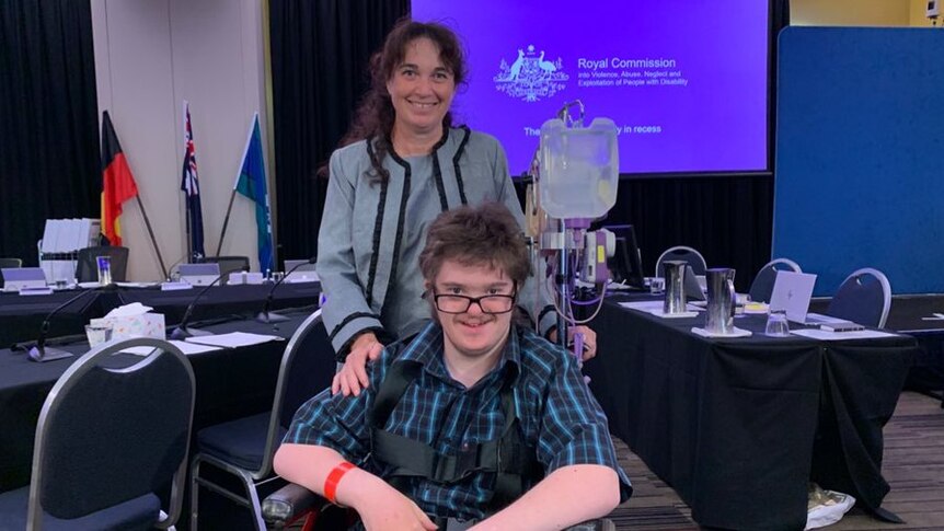 Toni Mitchell and her son Joshie, in a wheelchair, in front of a purple screen with disability royal commission information