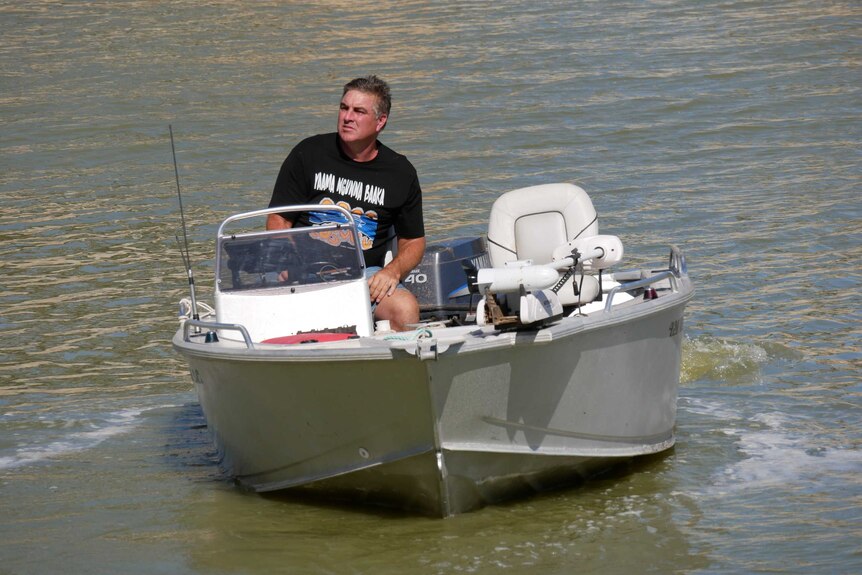A man in a black t-shirt driving a motorboat.