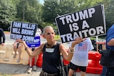 A man in a black T-shirt holds signs saying "Trump is a traitor" and "Fani Willis will bring Trump down"