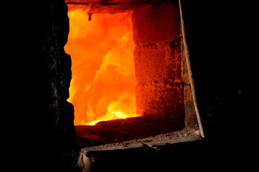 Flames and a pot through a small opening of a brick kiln.