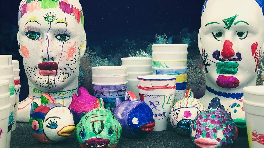 Polystyrene heads, fish and cups arranged on a table and decorated with coloured markers by children.