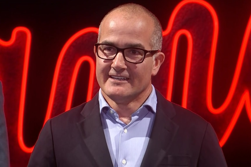 A man wearing a jacket, shirt and glasses speaking at media conference.