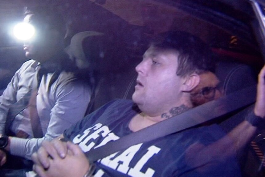 Jamie Saxon sits handcuffed in back of a police car.