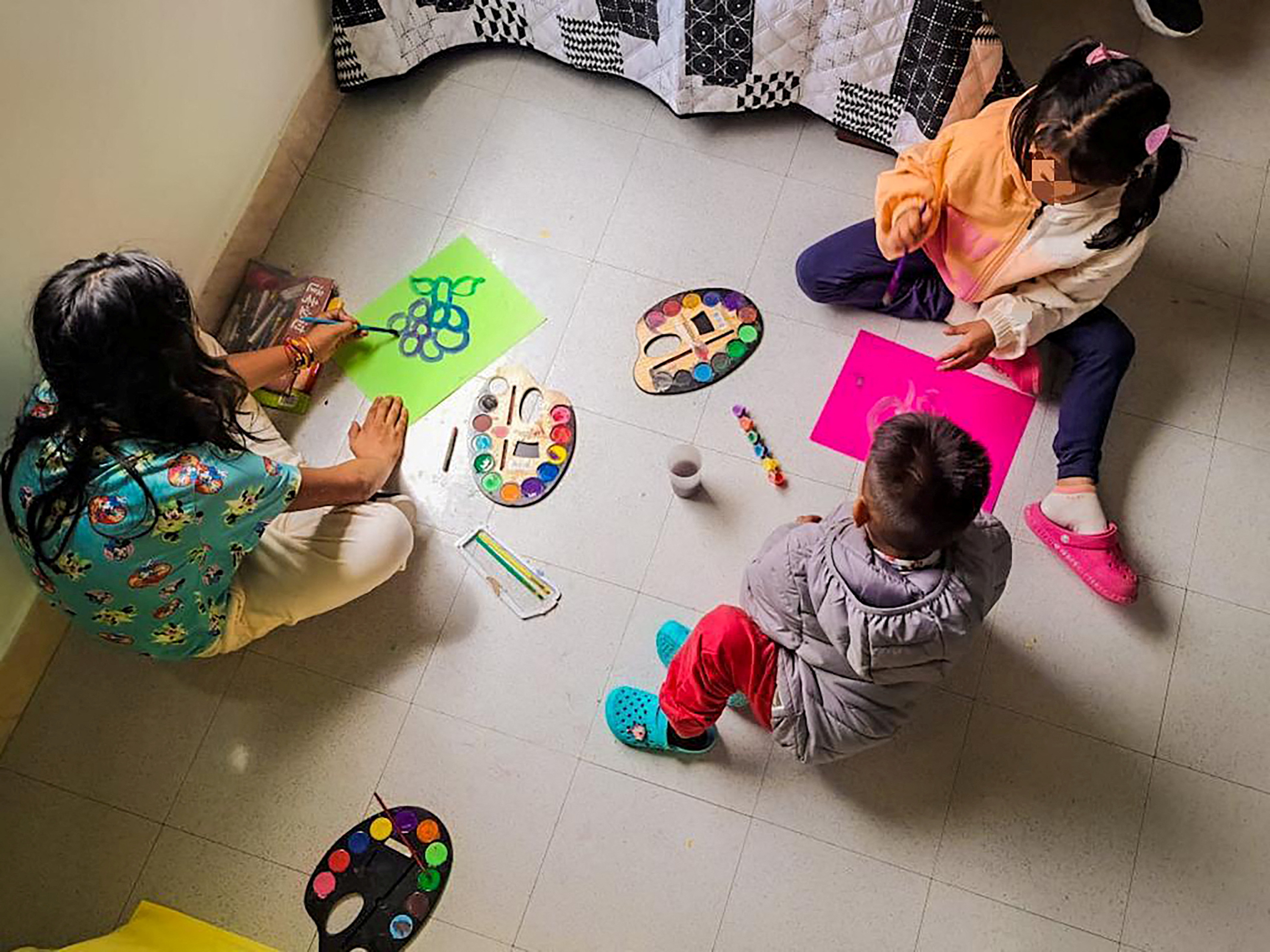 A photo taken from above shows children sat on the floor painting with bright colours.