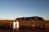 Two people standing in bathrobes look at Uluru at sunrise
