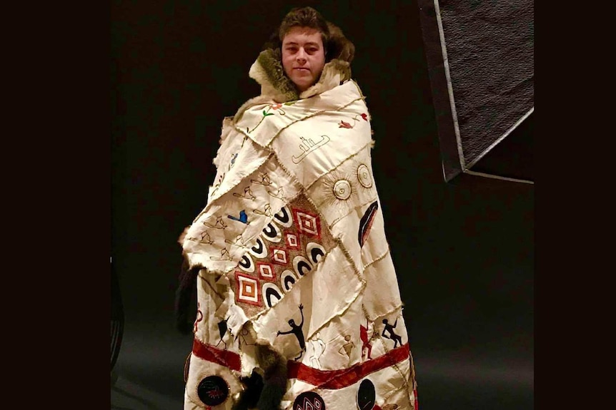 A young man wears a traditional possum skin cloak