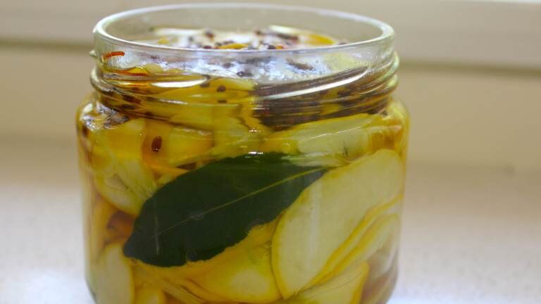 A jar of pickled yellow button squash with a bayleaf at the side of the jar.
