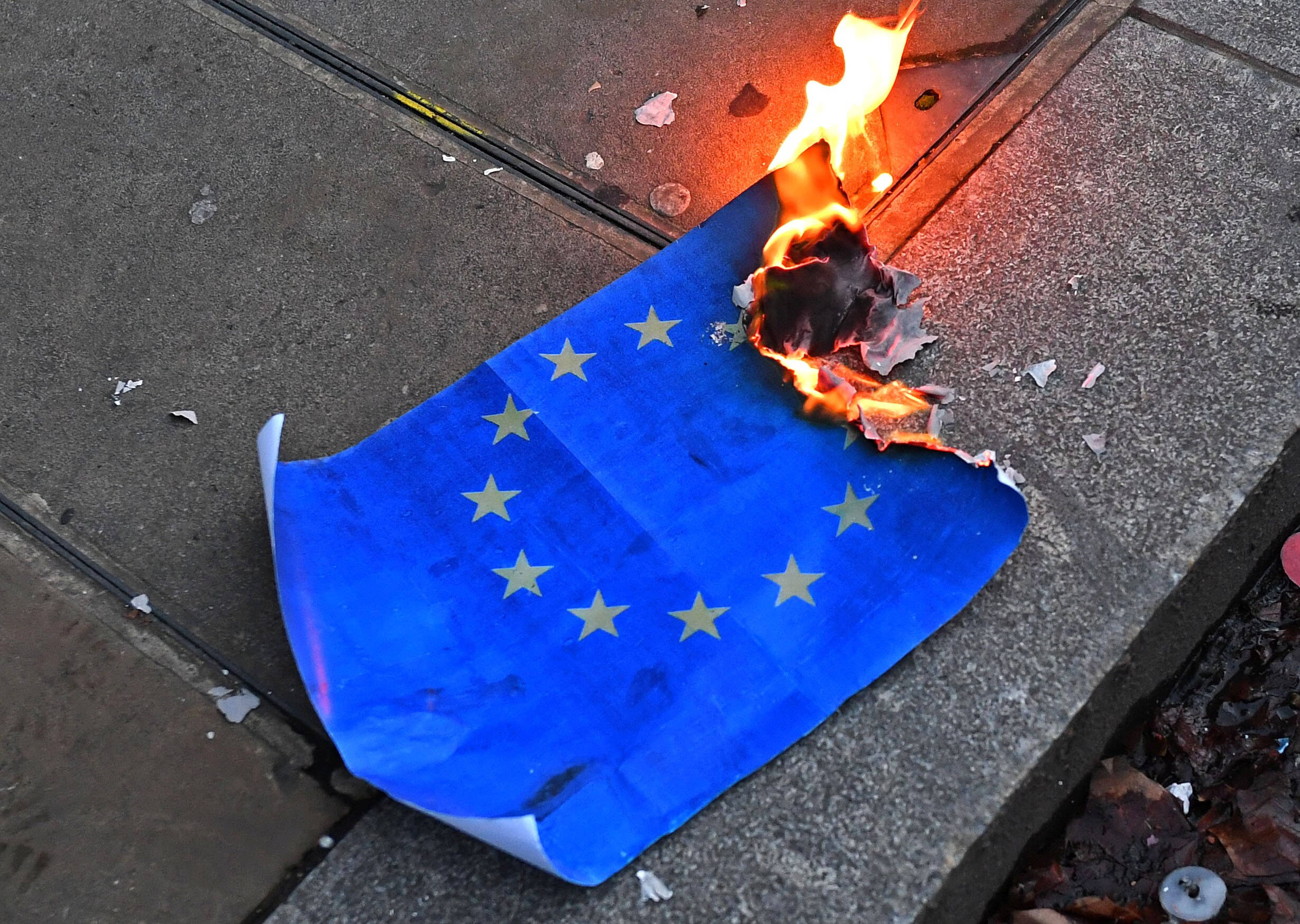 Close up of paper EU flag burning on pavement.