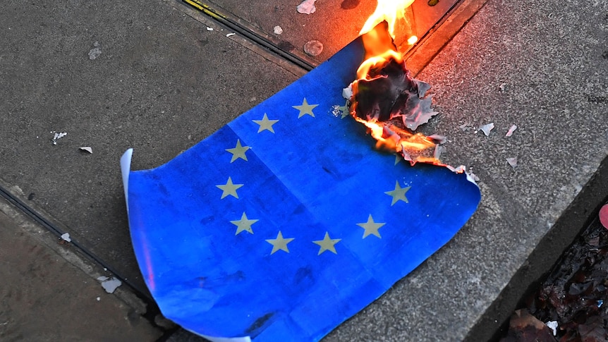 Close up of paper EU flag burning on pavement.