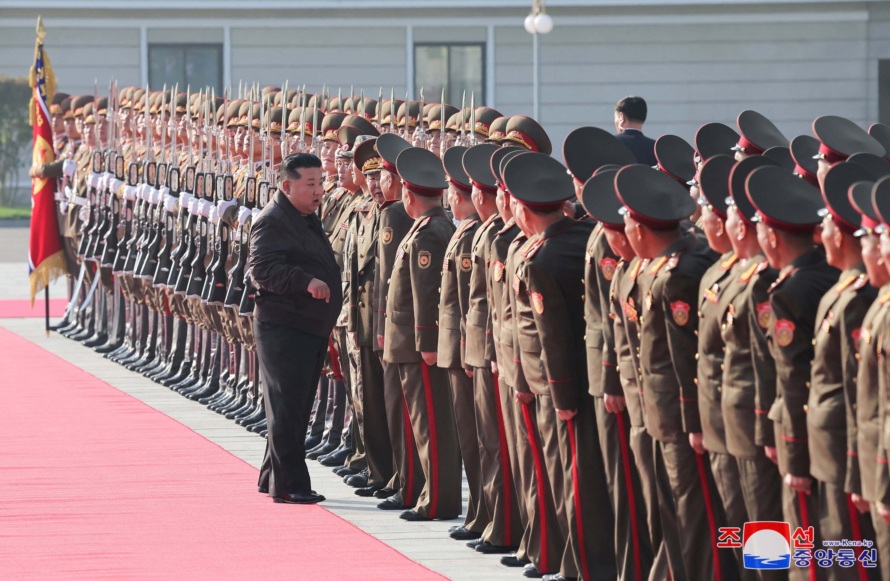 Kim Jong Un in a black suit standing in front of a line of dozens of North Korean soldiers wearing brown