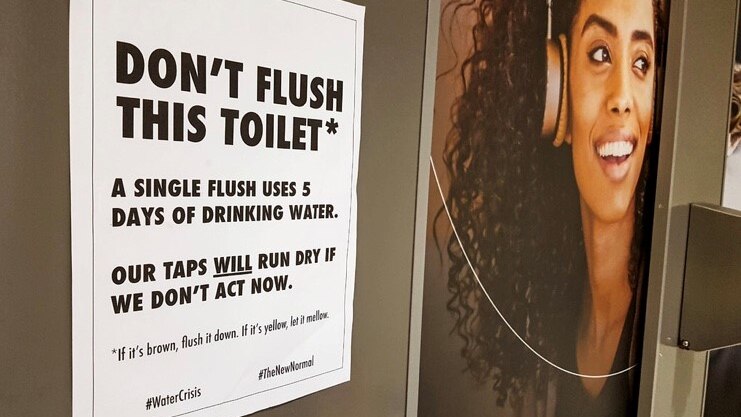 A sign inside Cape Town International Airport urging people not to flush the toilet, next to a picture of a woman.