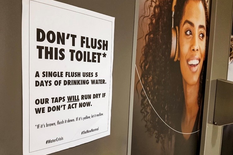 A sign inside Cape Town International Airport urging people not to flush the toilet, next to a picture of a woman.