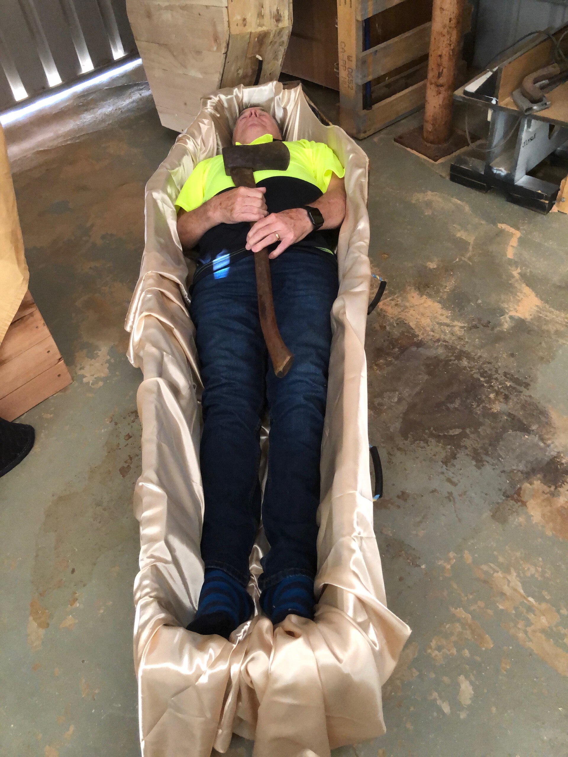 A man lying in a coffin with an axe