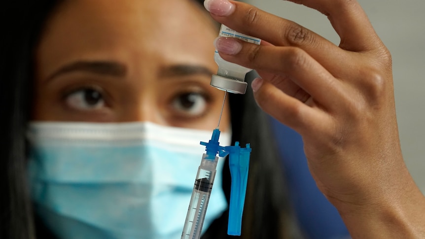 A healthcare worker wearing a face mask draws COVID-19 vaccine into a syringe