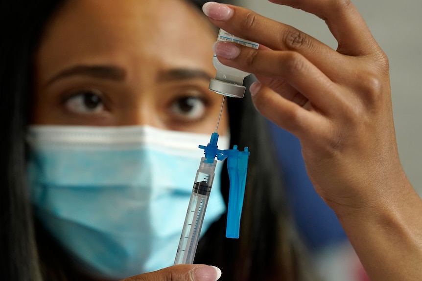 A healthcare worker wearing a face mask draws COVID-19 vaccine into a syringe