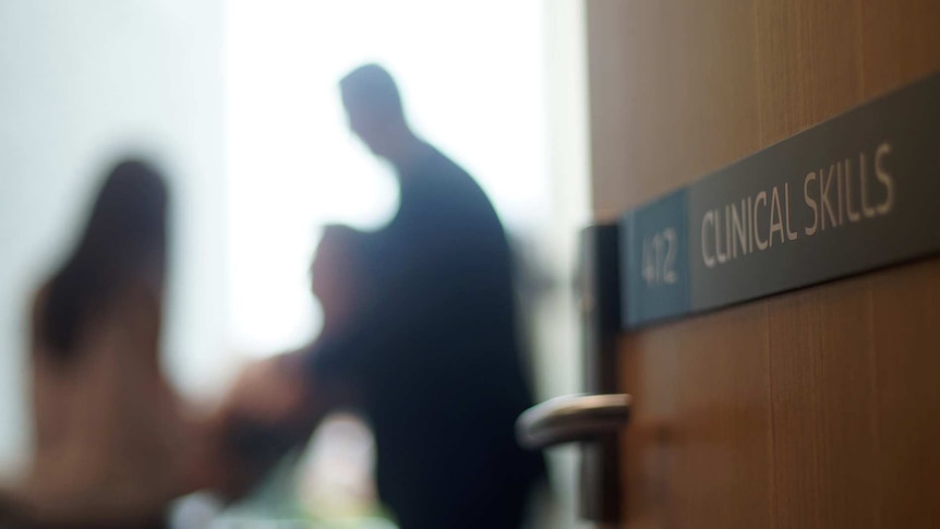 Blurred image of a doctor with a patient with a door marked "clinical skills" in the foreground.