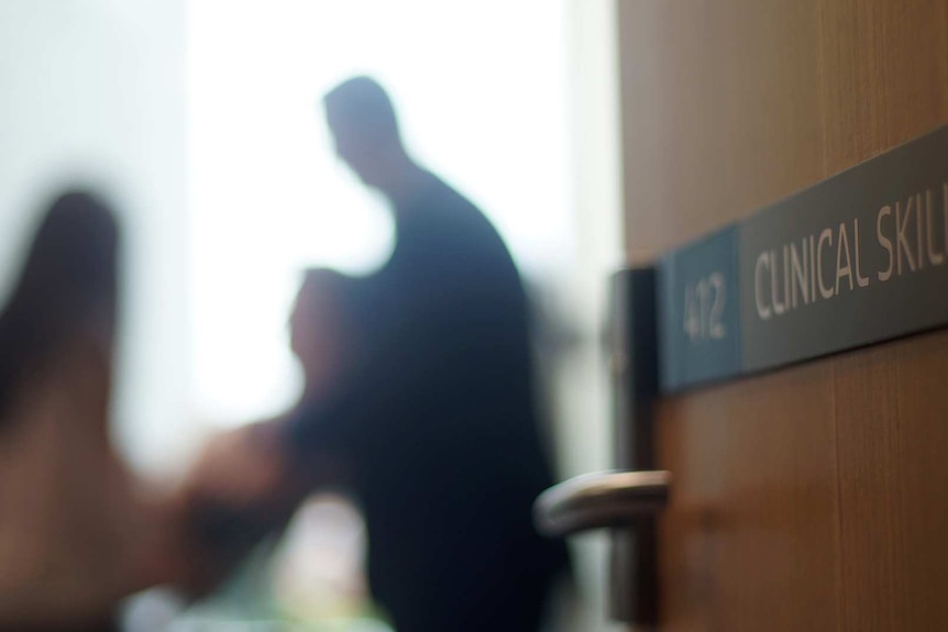 Blurred image of a doctor with a patient at the Curtin Medical School with a door marked "clinical skills" in the foreground.