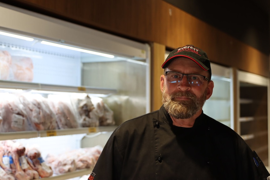 A man stands in front of a meat freezer looking sad.