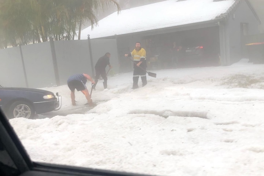 People stand digging through hailstones, which cover the ground in white.