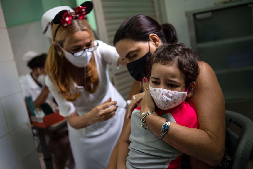A nurse in animal ears gives a vaccine to a child as their mother holds them. 
