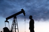 Silhouette of an oil well pumpjack and worker as night falls