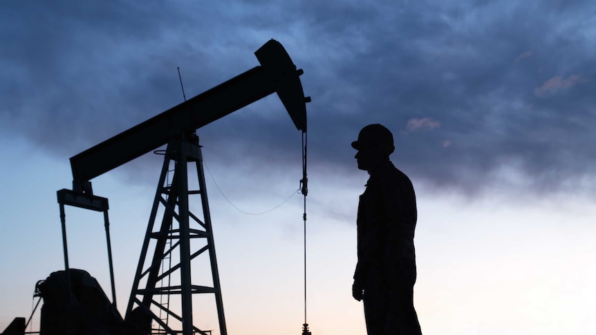 Silhouette of an oil well pumpjack and worker as night falls