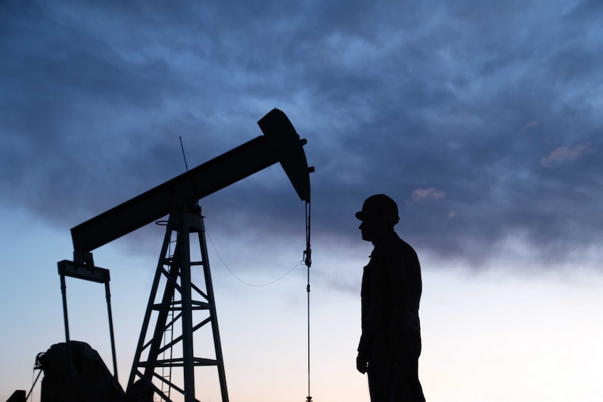 Silhouette of an oil well pumpjack and worker as night falls