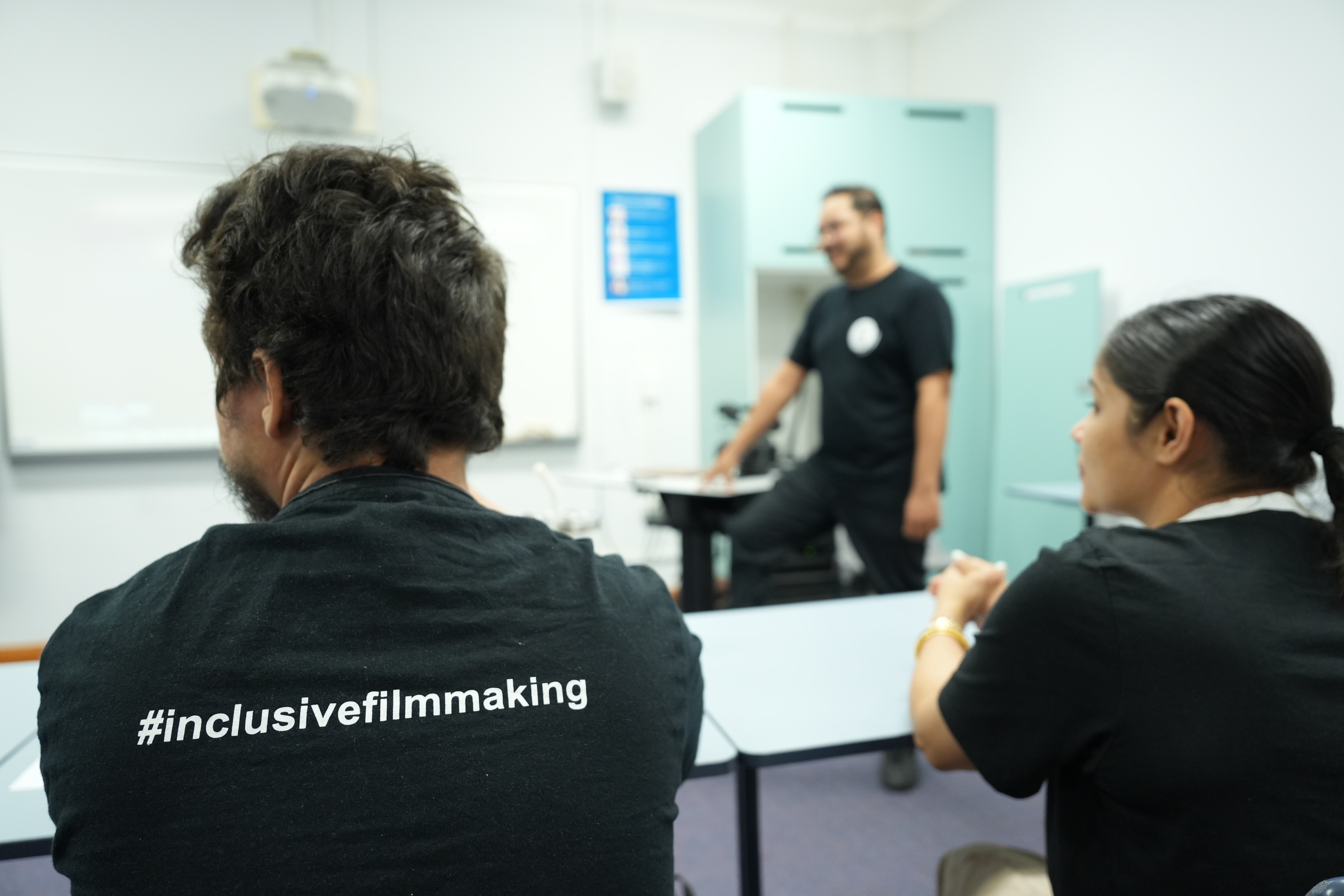 Dois estudantes vestindo camisetas que dizem cinema inclusivo sentados em uma sala de aula.