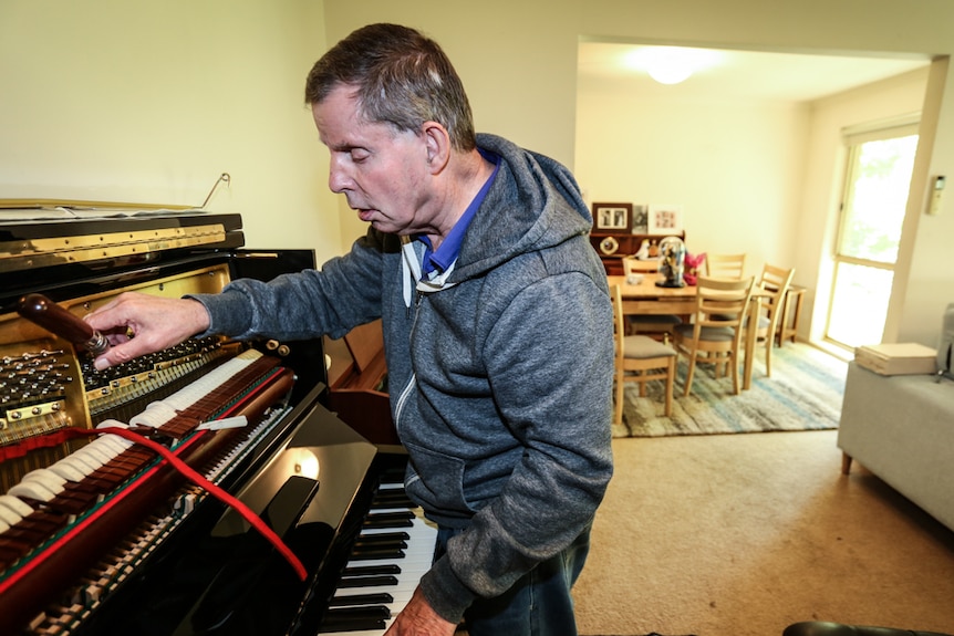 Graeme McGowan bending over an opened piano with his right hand on the tuning hammer and his left hand on the keys.