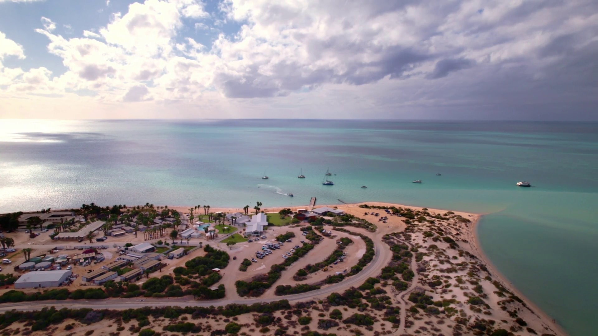 A vista de pájaro de una pequeña playa de arena y un mar azul claro.