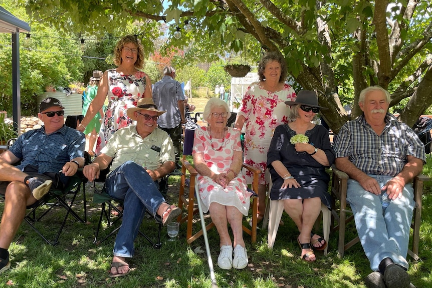 Five people sit down on chairs and two people stand up behind them in a garden