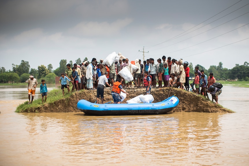 A large groups of villagers gather on a mound of land surrounded by water