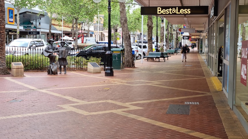 One person walks a long a footpath in Tamworth with several shops on the right-hand side.