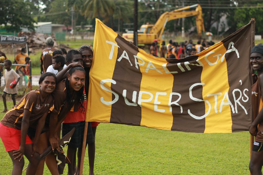 Tapalinga Superstars fans standing with a brown and yellow team banner.