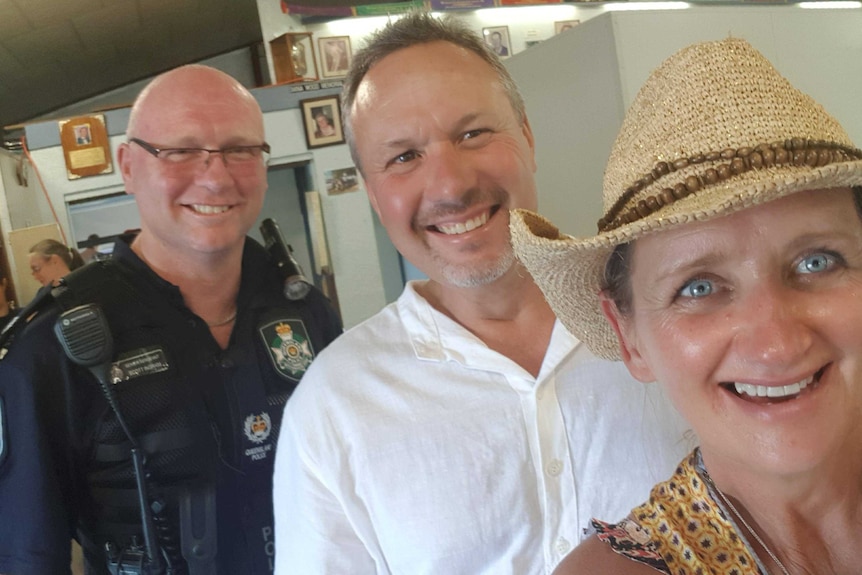 A policeman, a man, and a woman smile at the camera