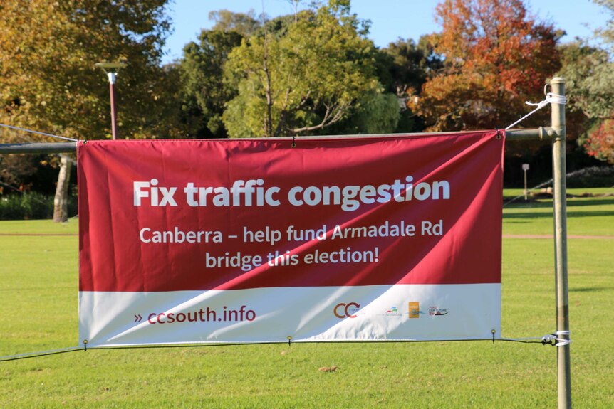 a red canvas banner reading 'Fix traffic congestion' hangs on posts in front of grass and trees.
