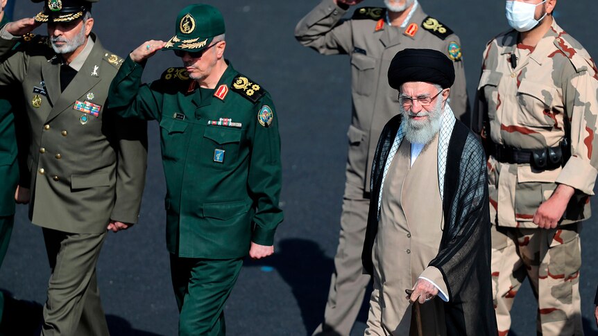 Iranian supreme leader Ayatollah Ali Khamenei walks alongside uniformed men saluting.