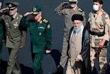 Iranian supreme leader Ayatollah Ali Khamenei walks alongside uniformed men saluting.