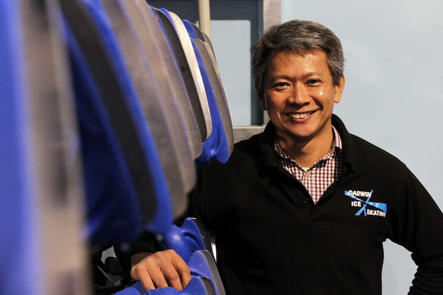 A man stands beside a rack with many pairs of ice skates.