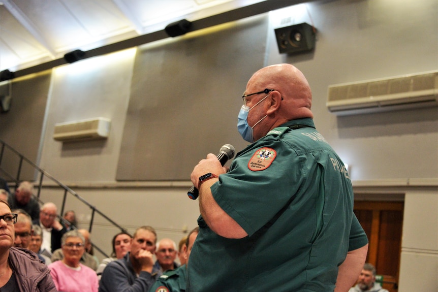 A man in an ambulance uniform holds a microphone addressing an audience 