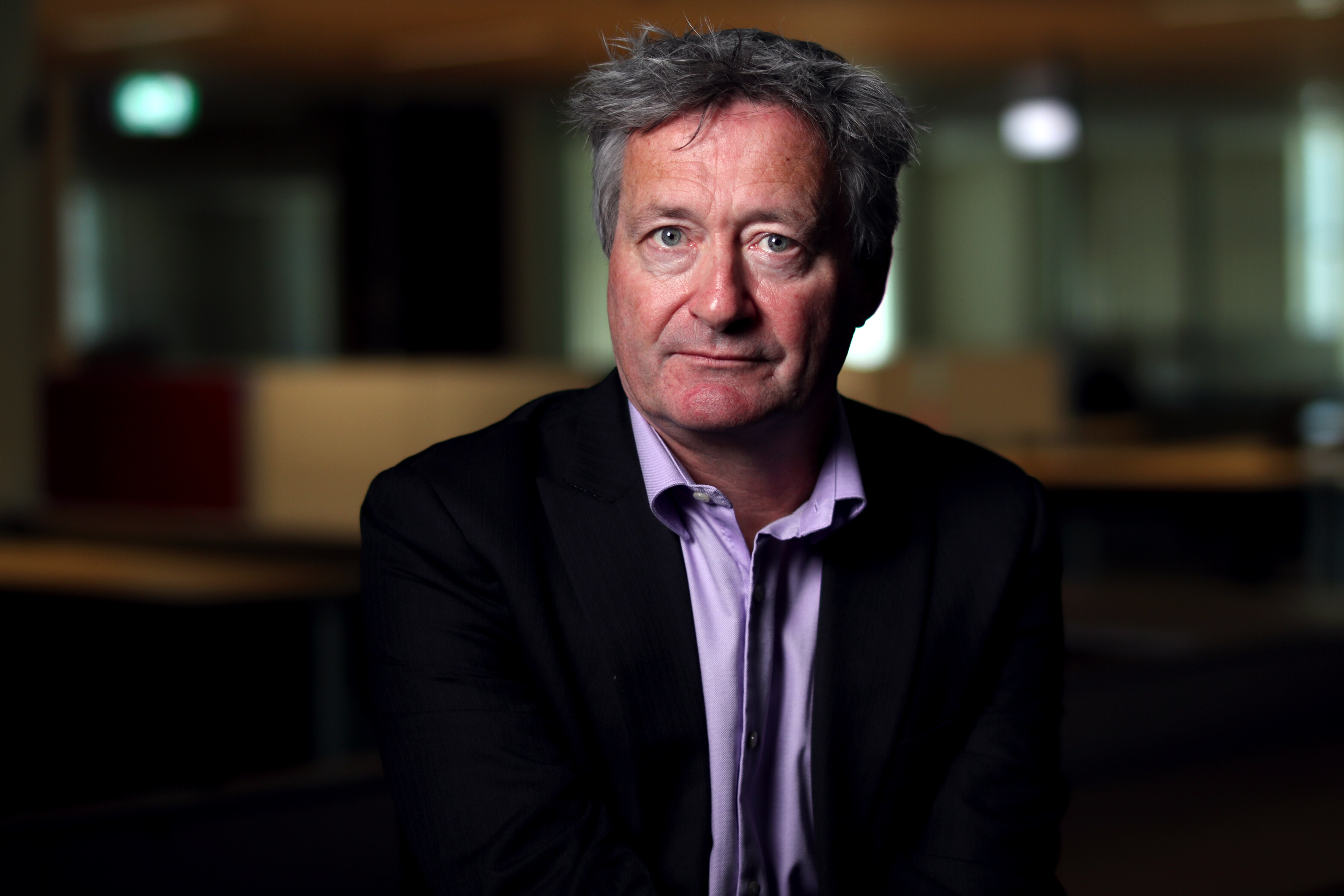 Gerard looks at the camera with a blank expression, sitting indoors.