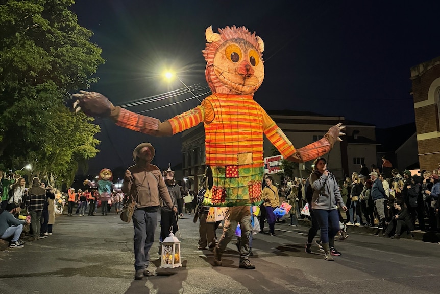 A giant lantern effigy of the beast from the book where the wild things are with long arms is walked along a street
