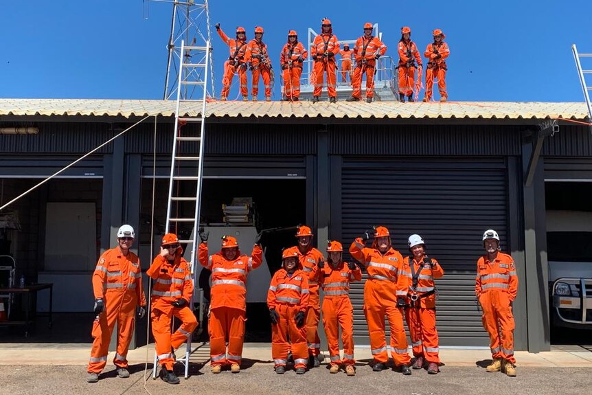 Volunteers dressed in orange stand on a garage roof and on the ground during training. A ladder leans against the garage. 
