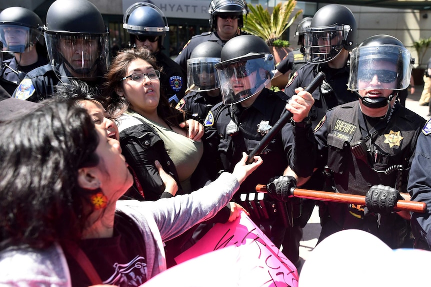 Police wearing helmets and vests hold back at least three female protesters