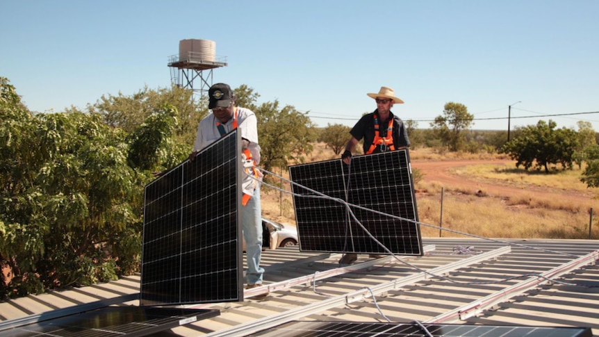 Two men install solar panels on a roof in a remote Aboriginal community
