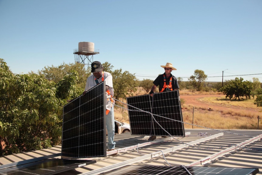 Two men install solar panels on a roof in a remote Aboriginal community