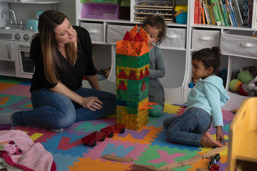 A woman sits on the floor playing with two little girls