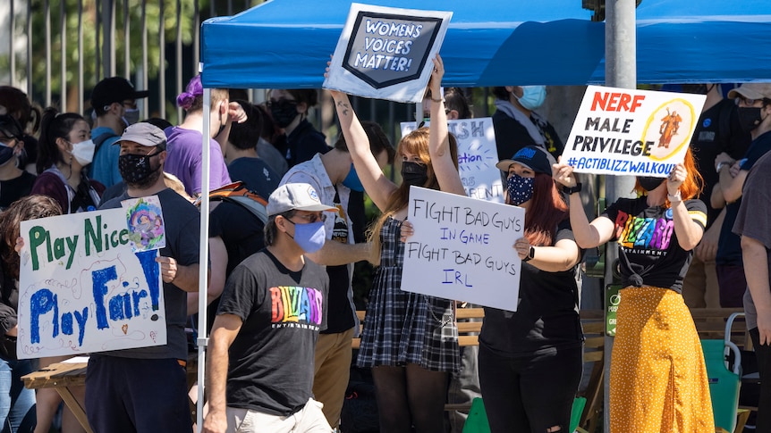 Women stand outside holding signs in protest against workplace discrimination. 