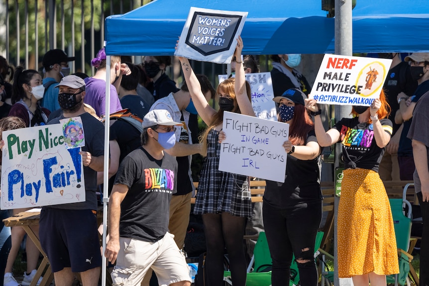 Women stand outside holding signs in protest against workplace discrimination. 