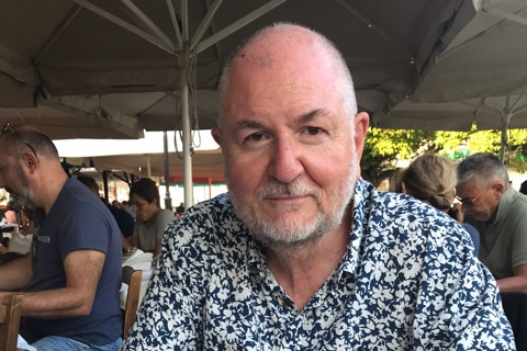 A man sits at a table with a beer in front of him.